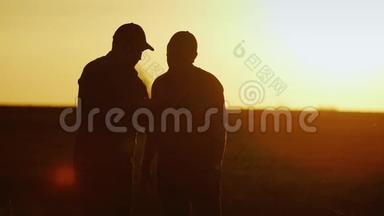 做农业综合企业的生意。 两个男农在田间交流，用平板握手. 日落时剪影